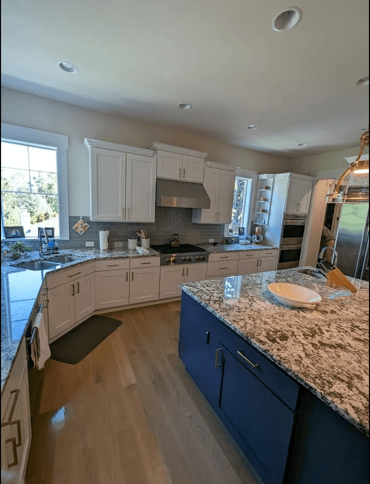 The same kitchen finished, warm white cabinets around a deep navy island under a granite worktop