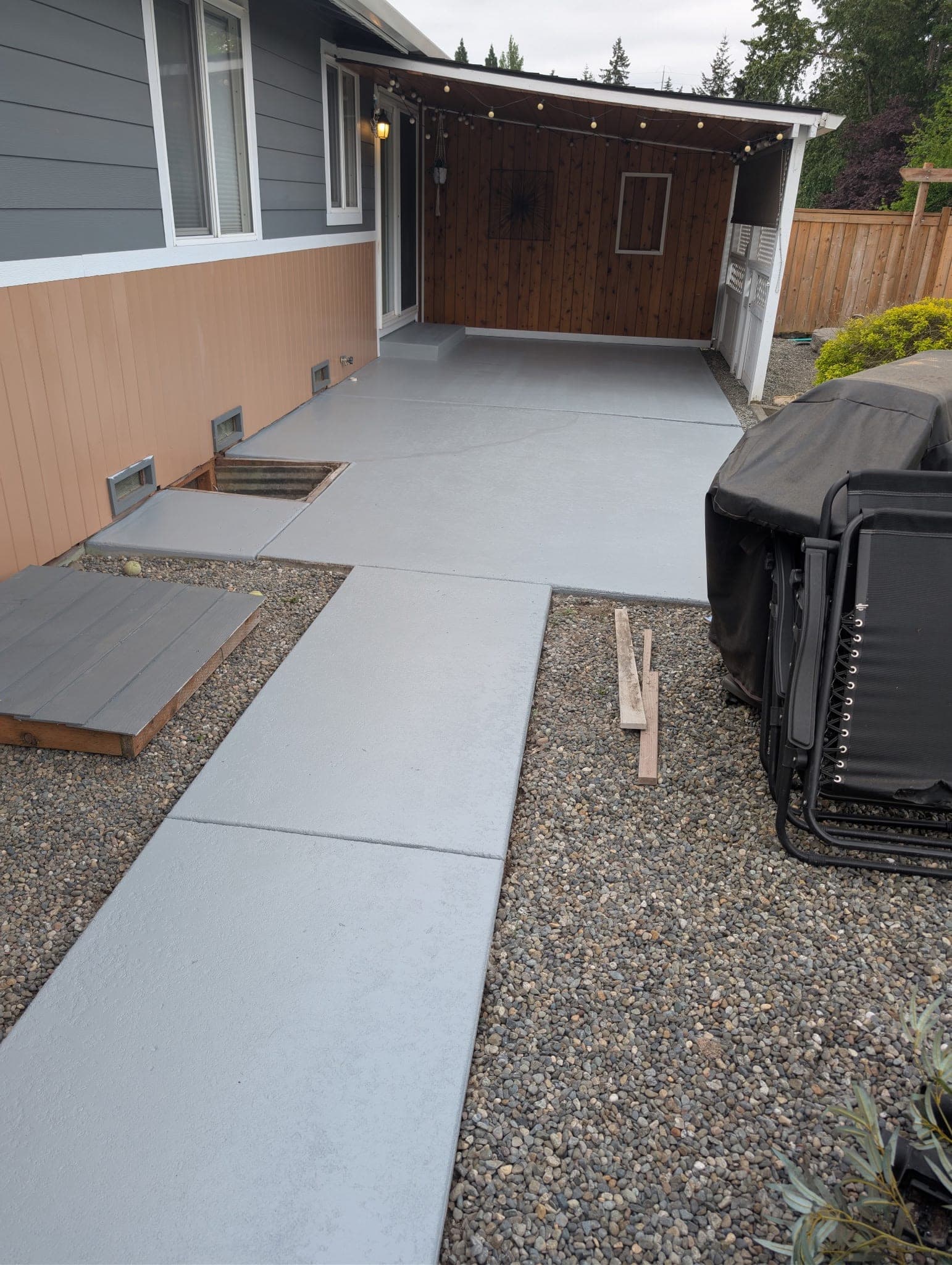 A finished patio and walkway in a uniform opaque light grey, under a cedar covered patio with string lights