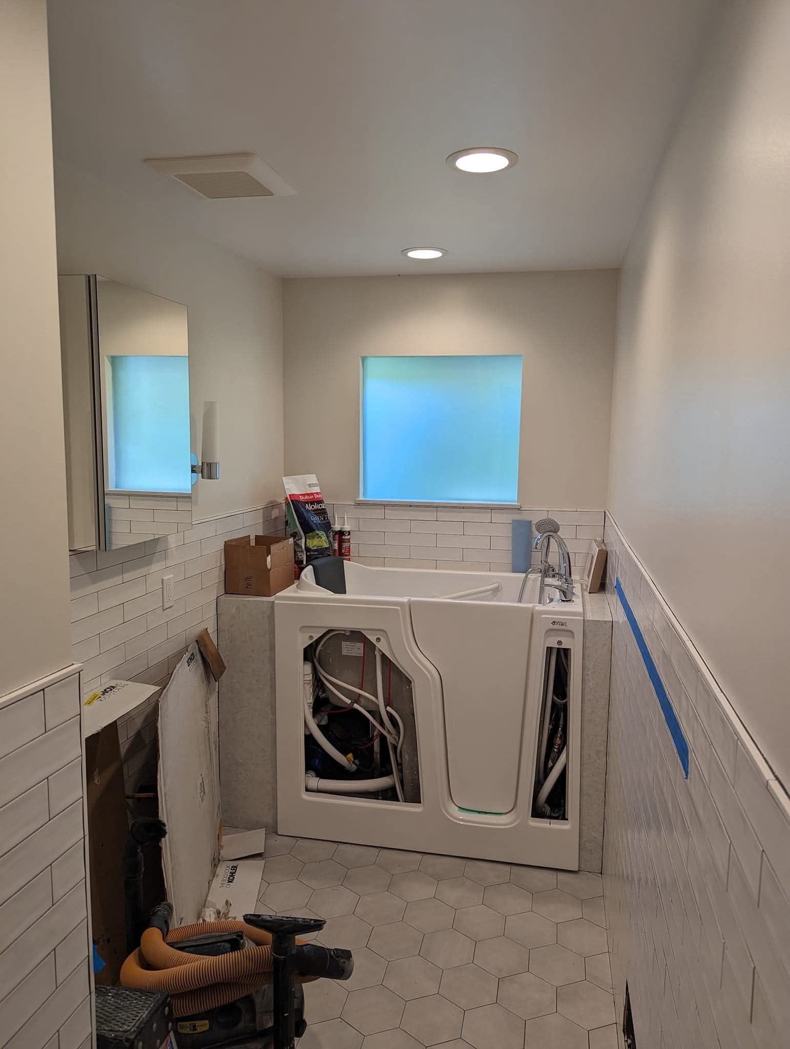 A bathroom mid-renovation with freshly painted walls and ceiling above white subway tile, a walk-in tub and hex floor tile
