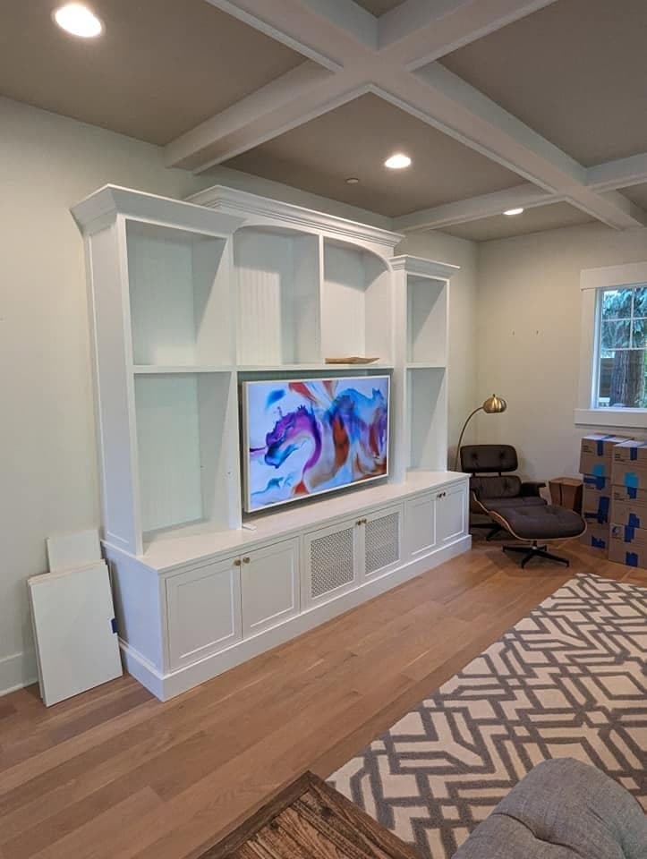 A large white built-in media wall with shelving under a coffered ceiling