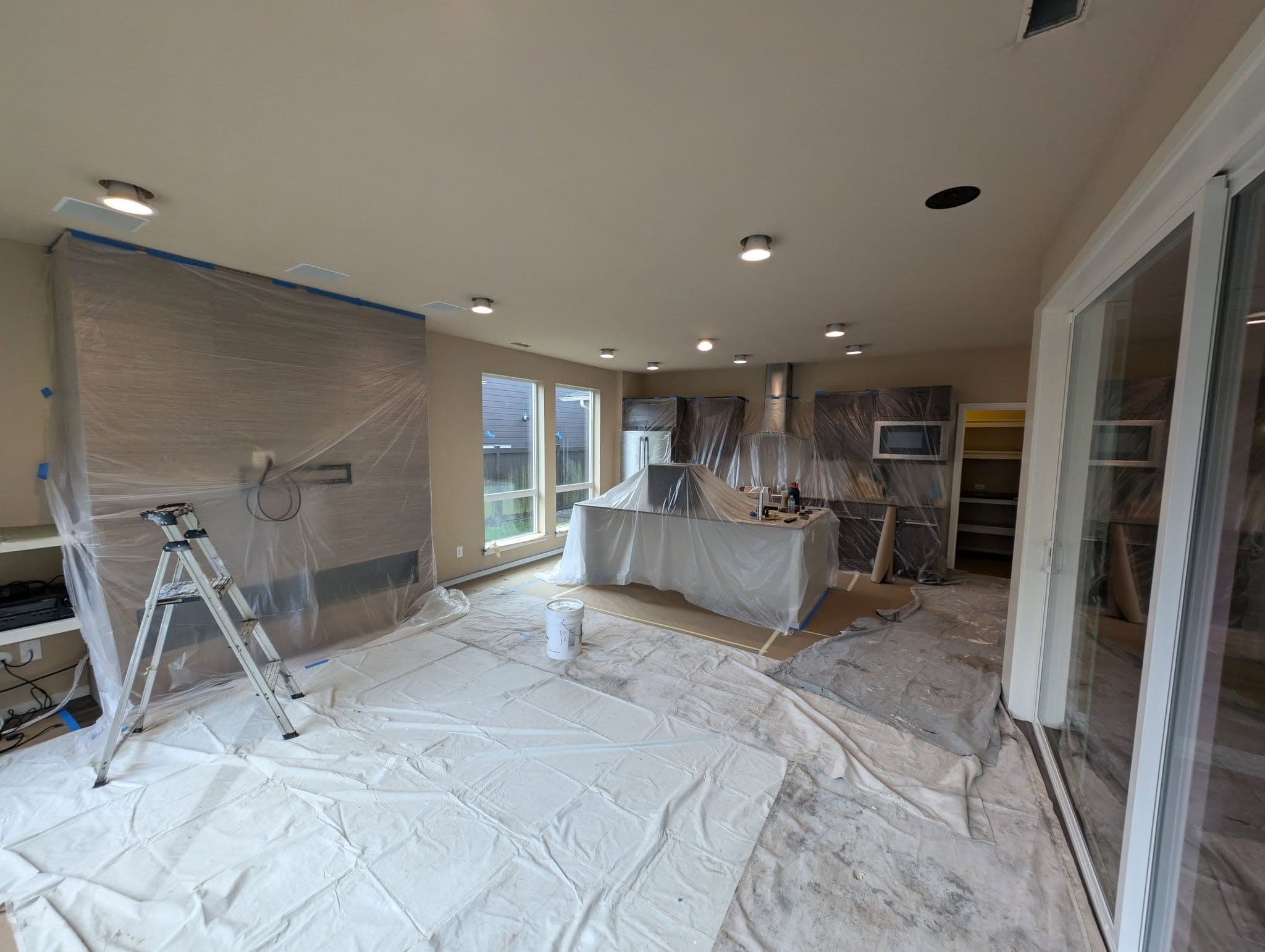 A kitchen fully masked for spraying with plastic over the cabinets and island and drop cloths across the floor