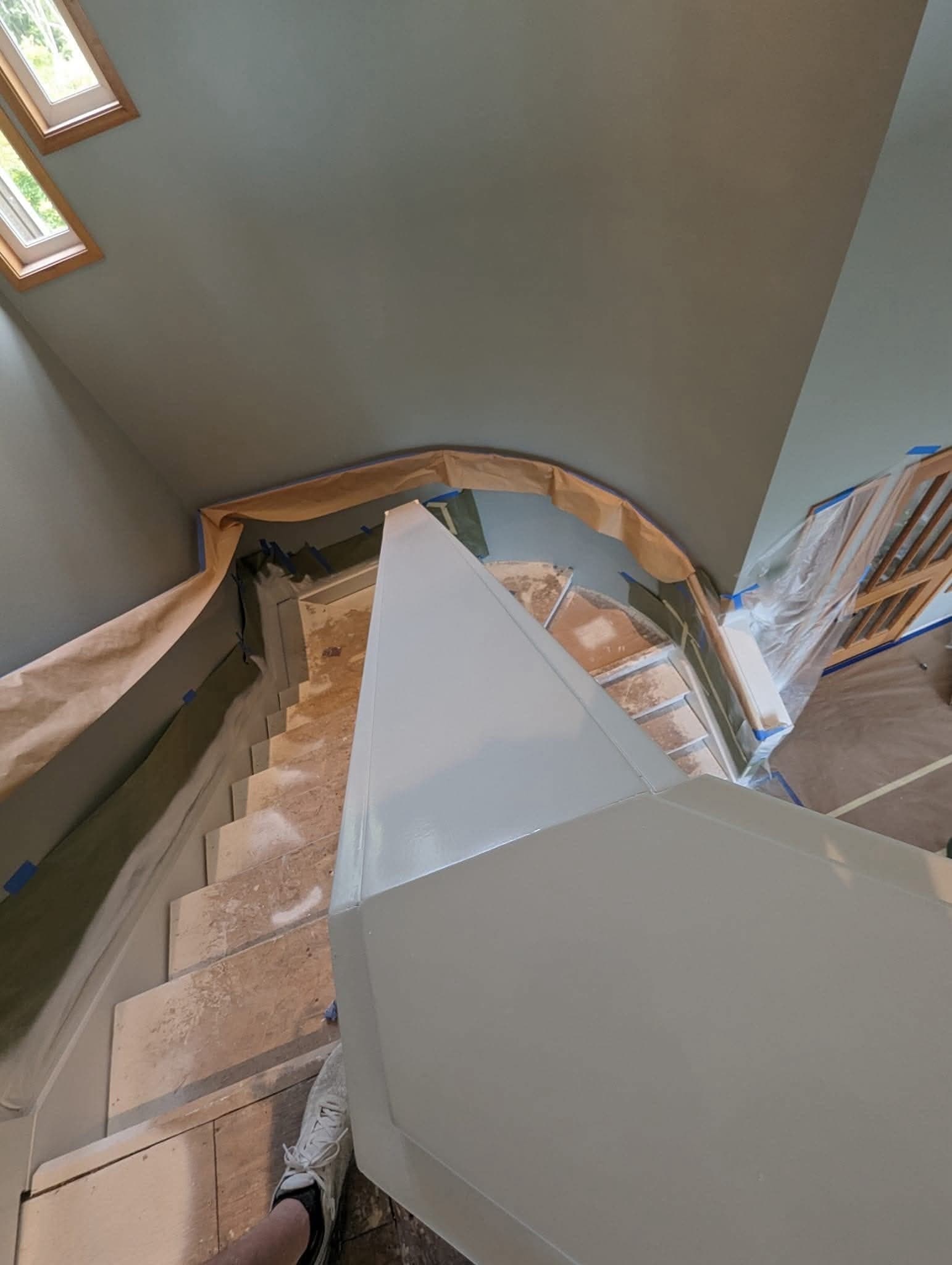 The same stairwell mid-job, skirt and newel coated, masking paper taped along the wall line and every tread covered