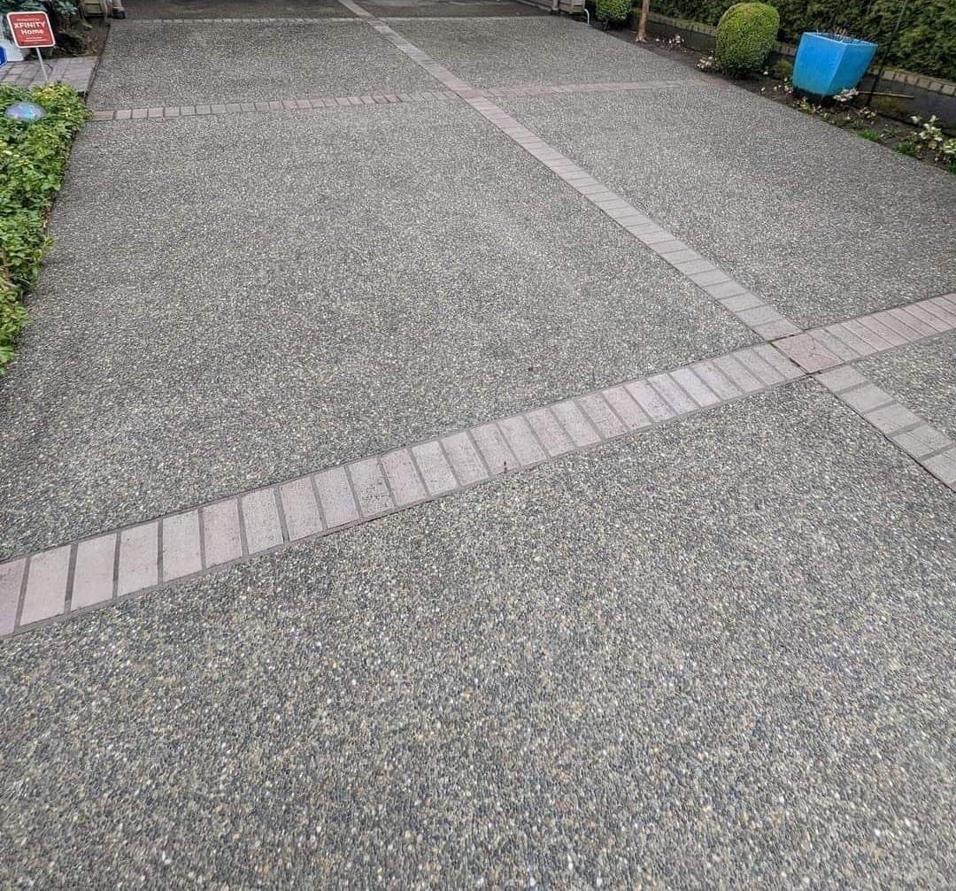 The same driveway finished, clean aggregate concrete with pink brick banding running through it