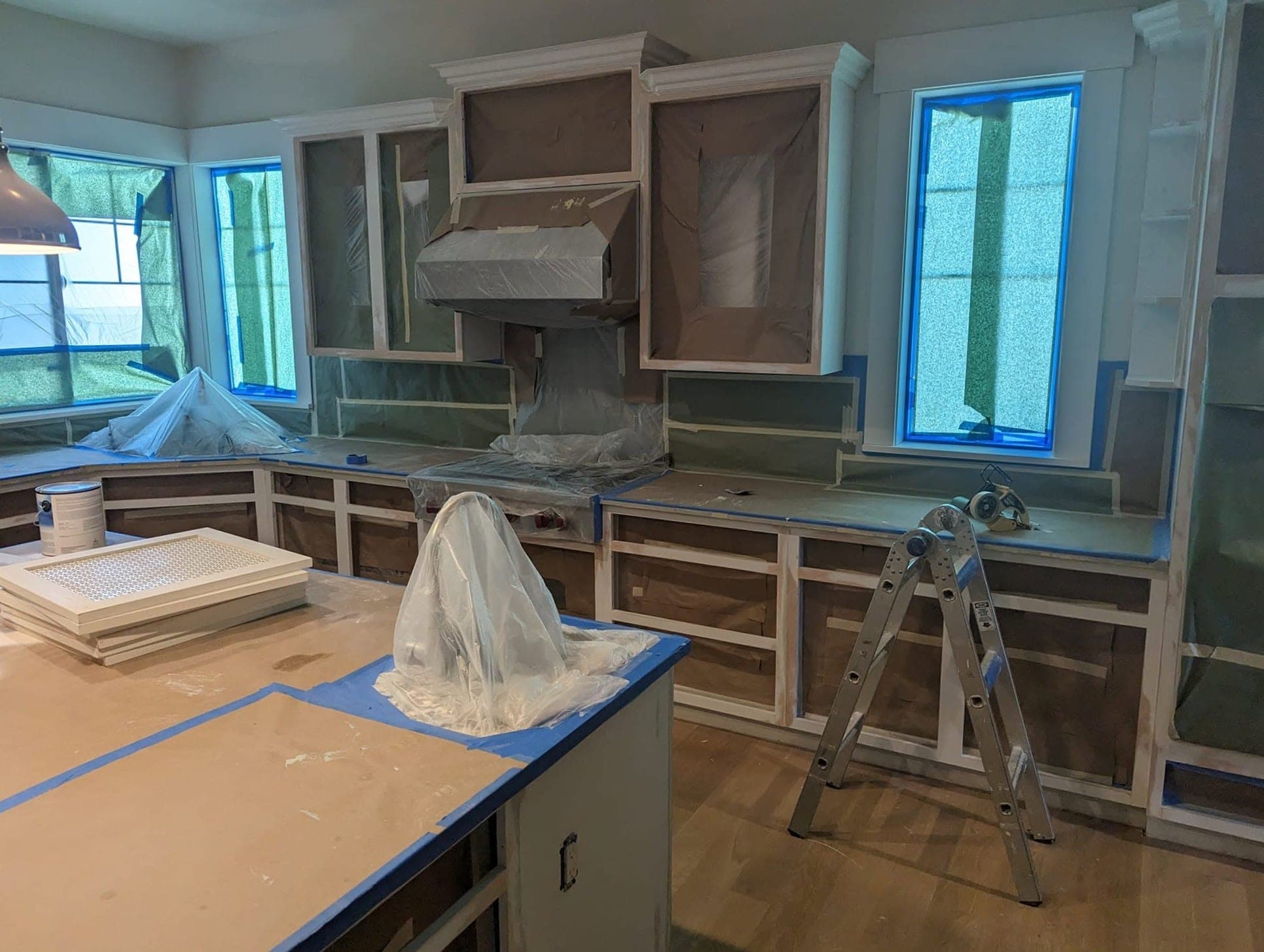 The kitchen masked for spraying, with paper over every cabinet front, the range hood bagged and the windows taped out