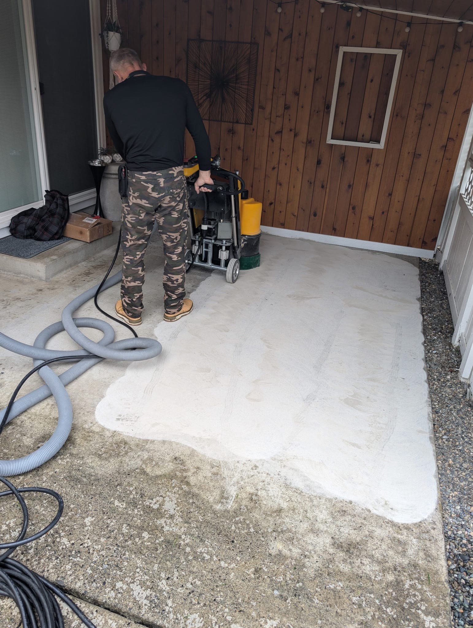 The same slab with a floor grinder halfway across it, half of it ground back to pale concrete and half still stained