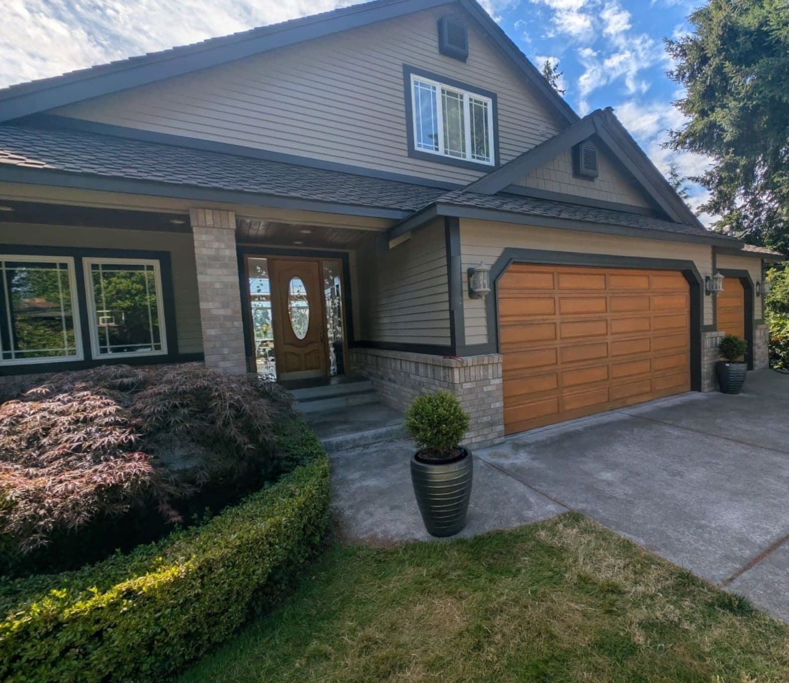 A finished two-story craftsman in warm grey siding with charcoal trim, brick columns and timber garage doors