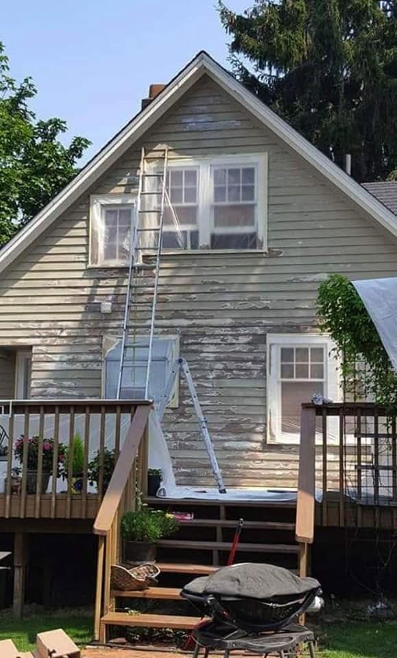 A gable end with paint peeling off in sheets and a ladder against the wall