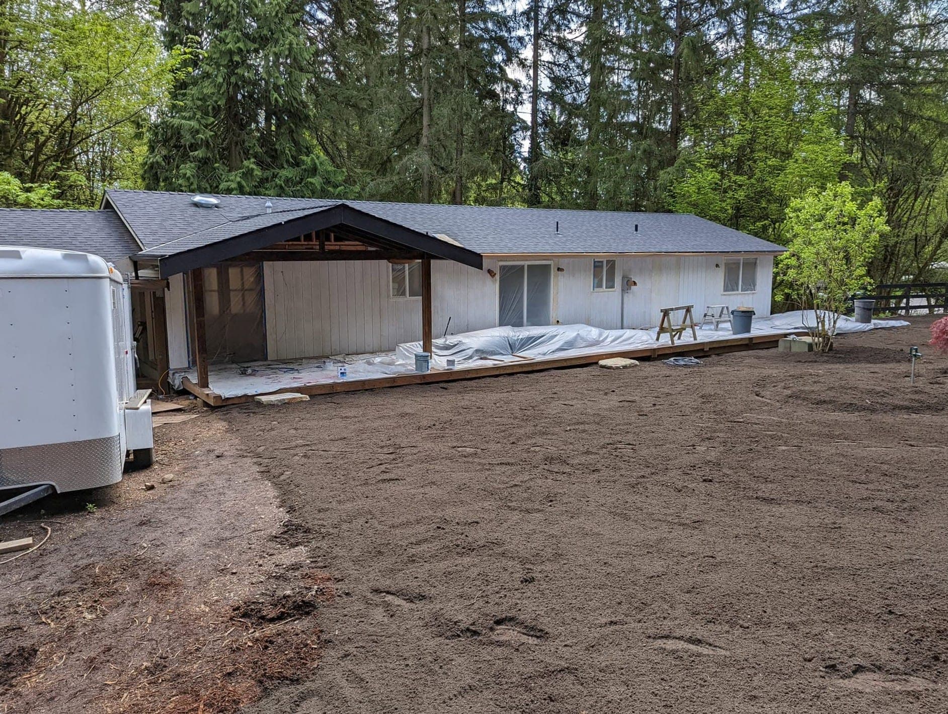 A long single-story ranch mid-job with bare siding, masked windows and plastic sheeting along the base of the wall