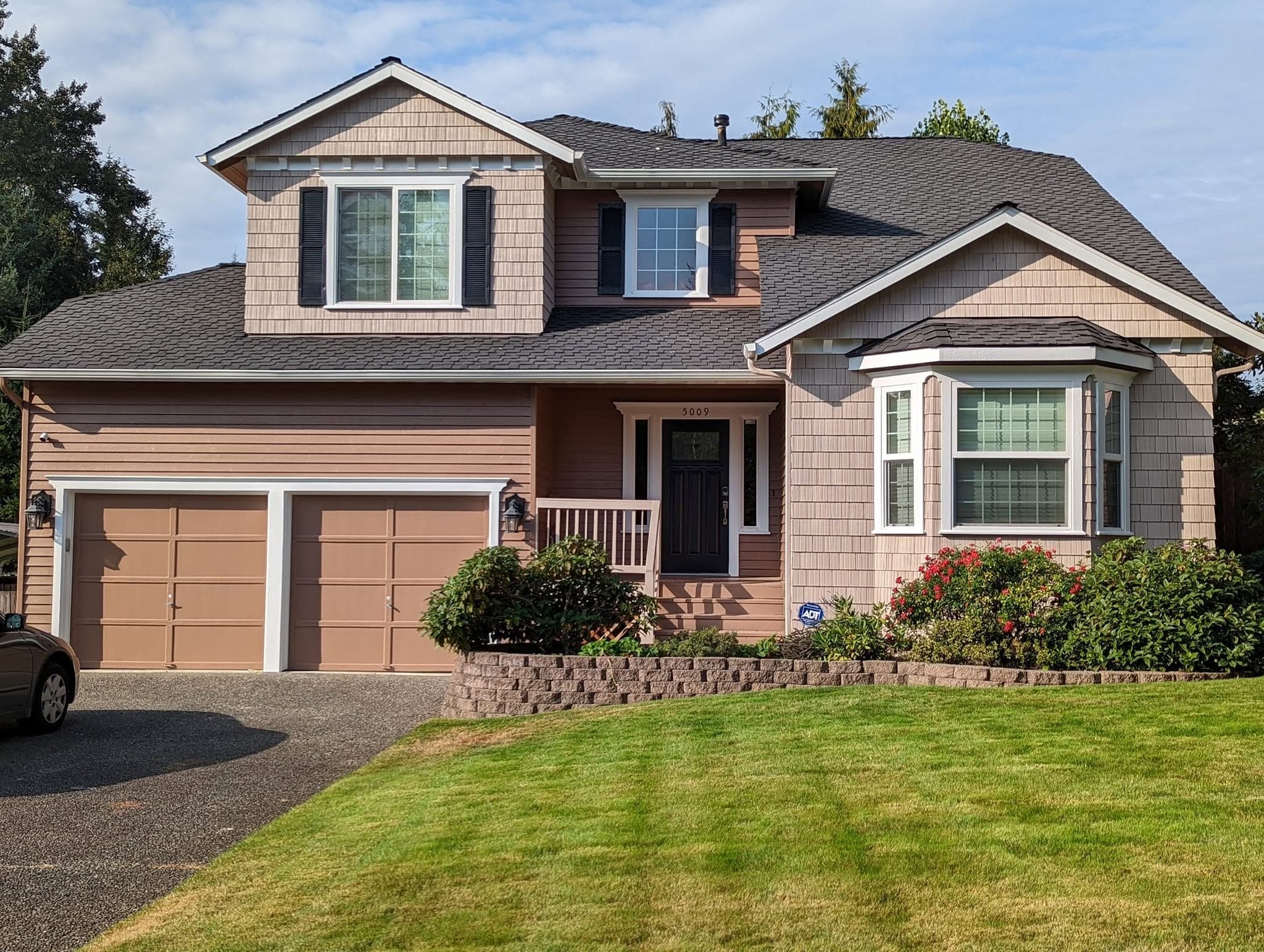 A freshly painted two-story craftsman home in tan and mocha, with a green front lawn under a blue sky