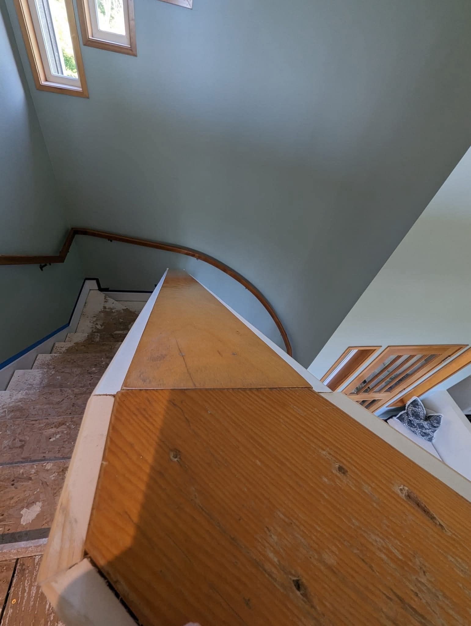 A stairwell before the millwork was painted, with a bare skirt board, the original stained handrail and treads stripped back