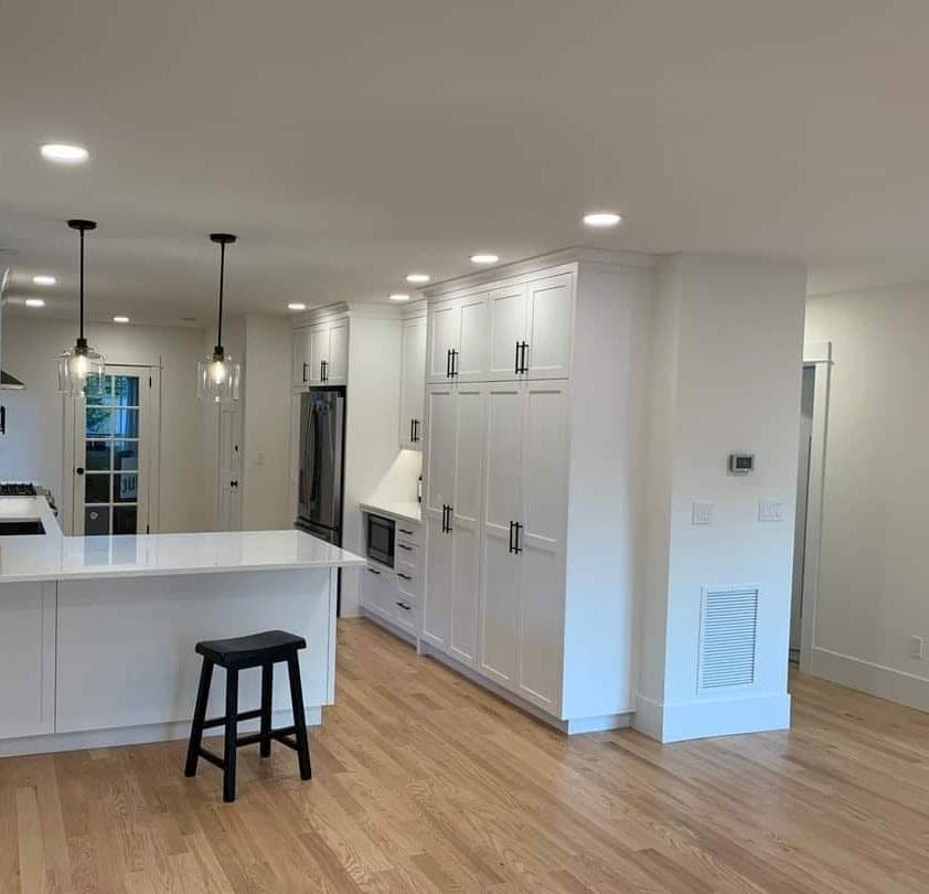 A bright open plan kitchen and living space with white cabinetry, fresh white walls and light oak floors